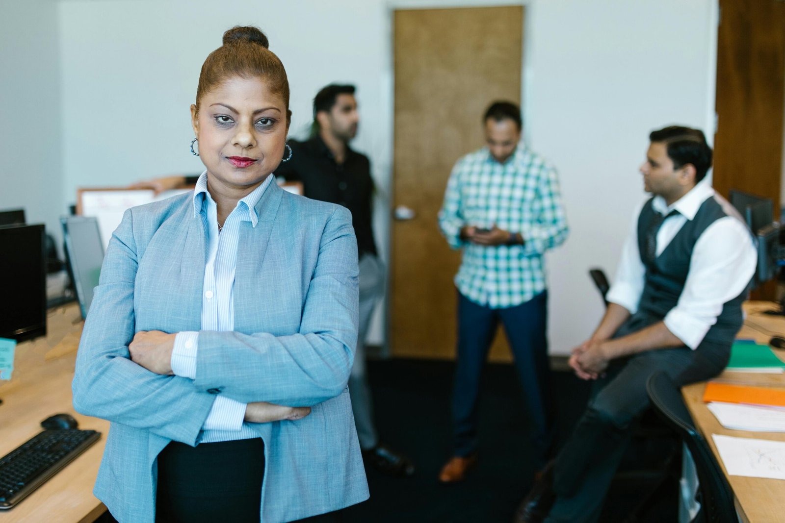 Confident businesswoman standing in modern office with colleagues in the background.