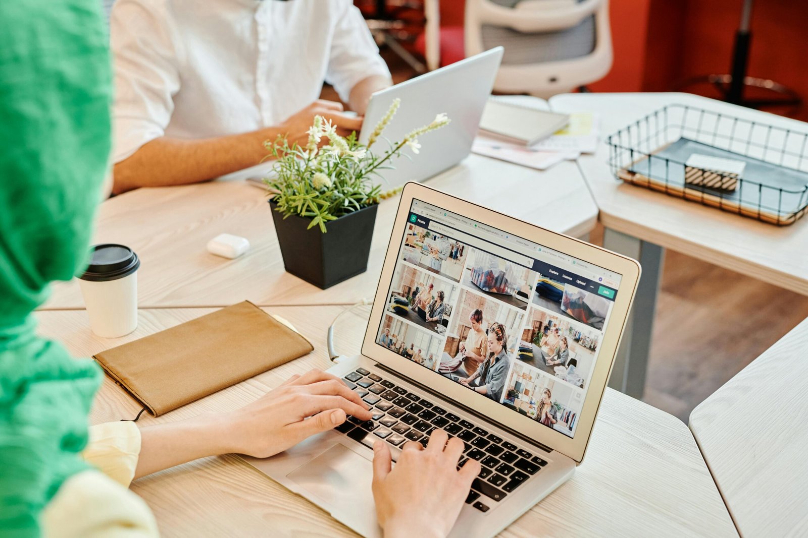 Professional using laptop at desk in a shared office with a focus on work environment.